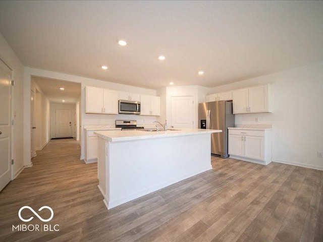 kitchen featuring sink, an island with sink, appliances with stainless steel finishes, light hardwood / wood-style floors, and white cabinetry