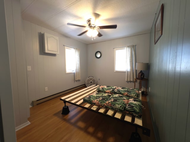 bedroom with wood-type flooring, multiple windows, a baseboard radiator, and ceiling fan