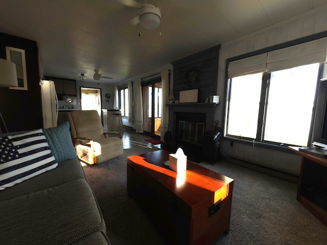 living room with dark colored carpet, baseboard heating, ceiling fan, and a fireplace