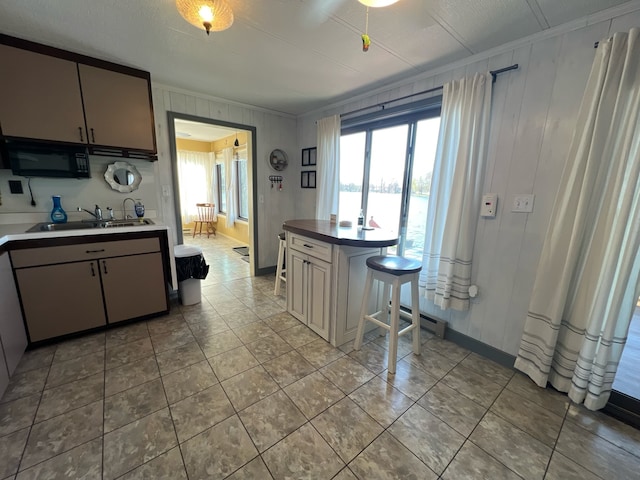 kitchen with light tile floors, sink, a breakfast bar area, ornamental molding, and a baseboard radiator