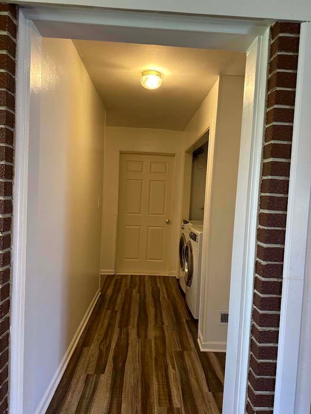 hall with washing machine and dryer, brick wall, and dark hardwood / wood-style floors