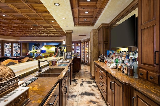 bar featuring decorative columns, sink, dark stone countertops, and light tile flooring