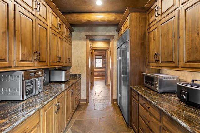 kitchen with built in fridge, dark tile floors, and dark stone countertops