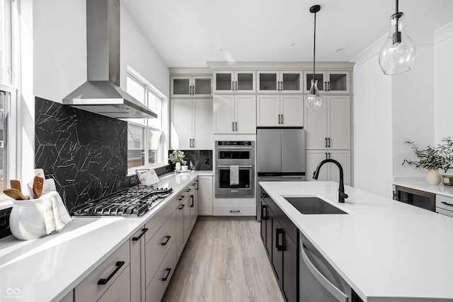 kitchen featuring hanging light fixtures, stainless steel appliances, sink, white cabinetry, and wall chimney range hood