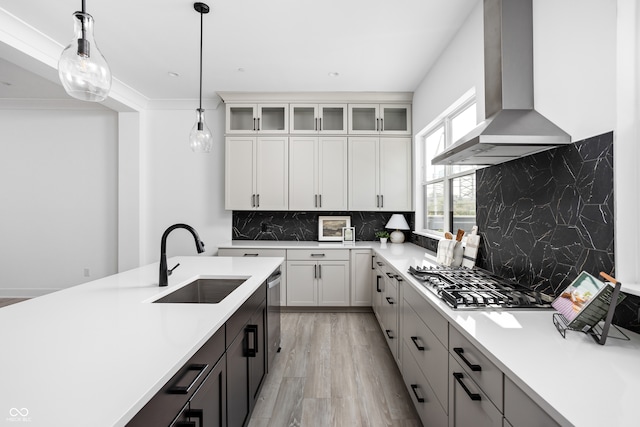 kitchen with backsplash, decorative light fixtures, sink, white cabinets, and wall chimney range hood