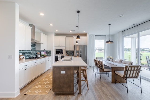 kitchen featuring decorative light fixtures, a breakfast bar, appliances with stainless steel finishes, wall chimney range hood, and a center island with sink