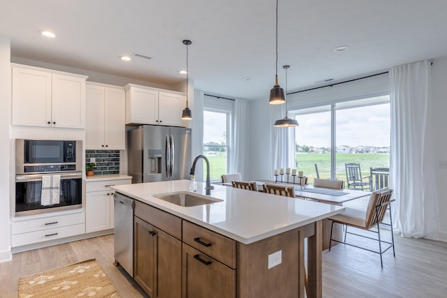 kitchen featuring decorative light fixtures, a center island with sink, white cabinets, and stainless steel appliances