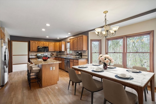 kitchen with appliances with stainless steel finishes, a center island, tasteful backsplash, and light wood-type flooring