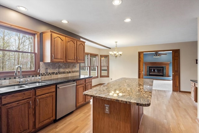 kitchen featuring light wood-type flooring, a kitchen island, stainless steel dishwasher, hanging light fixtures, and sink