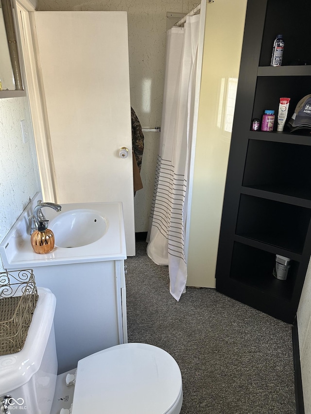 full bath featuring toilet, vanity, and a textured wall