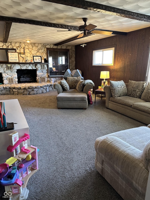 carpeted living room featuring wood walls, a fireplace, beam ceiling, and a ceiling fan