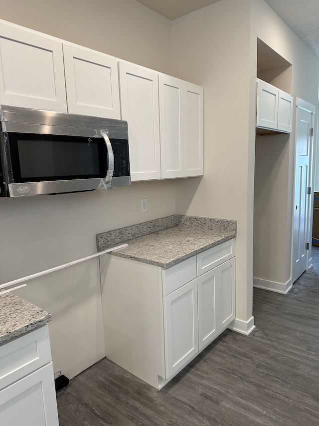 kitchen with light stone counters, dark hardwood / wood-style flooring, and white cabinets