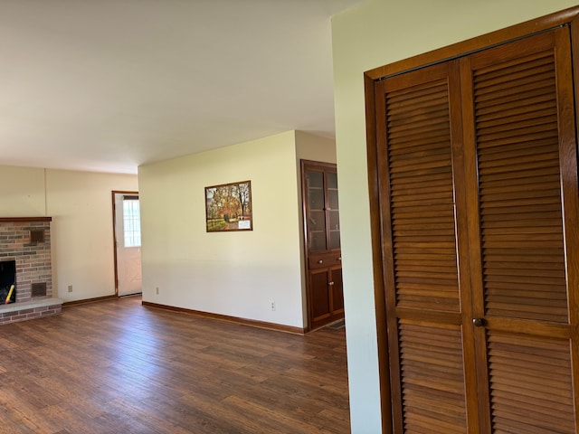 unfurnished living room featuring a brick fireplace and dark wood-type flooring