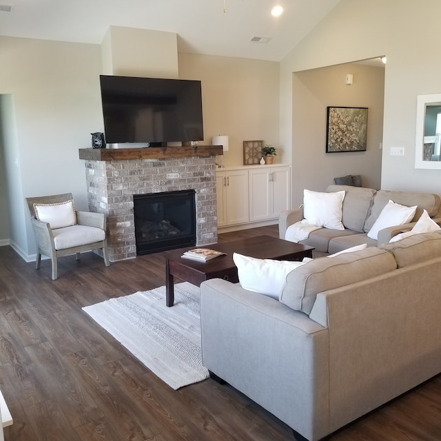 living room with high vaulted ceiling, a brick fireplace, and dark wood-type flooring