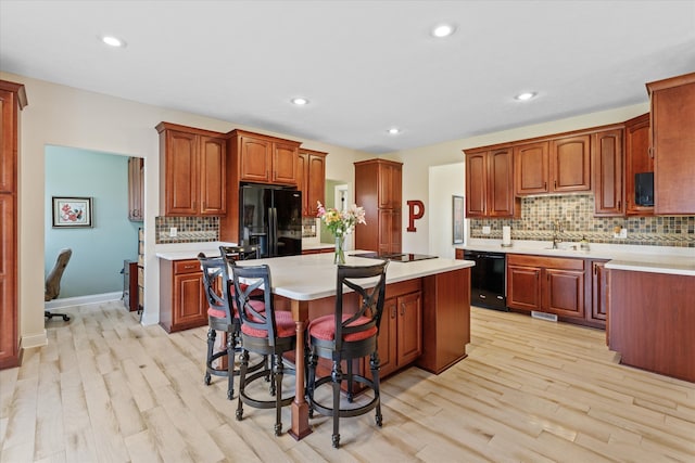 kitchen with light hardwood / wood-style flooring, backsplash, a kitchen island, and black appliances