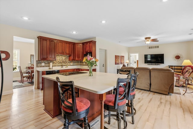 kitchen with light wood-type flooring, backsplash, a breakfast bar area, black electric cooktop, and ceiling fan