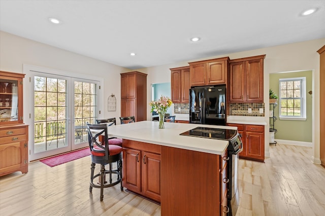 kitchen featuring light hardwood / wood-style floors, backsplash, black fridge with ice dispenser, range with electric stovetop, and a kitchen island with sink