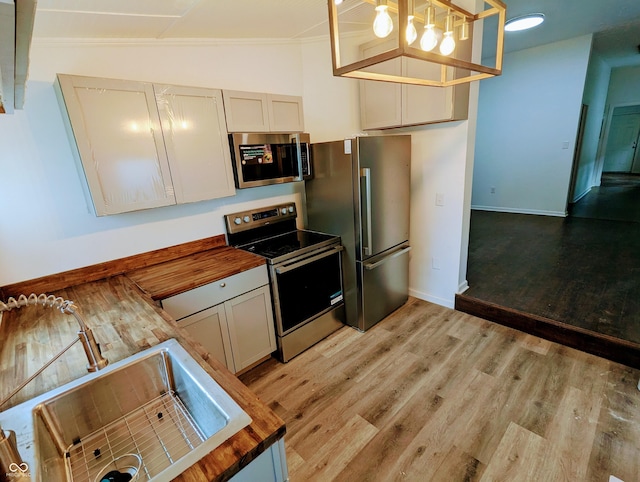 kitchen featuring wooden counters, light hardwood / wood-style floors, vaulted ceiling, decorative light fixtures, and appliances with stainless steel finishes