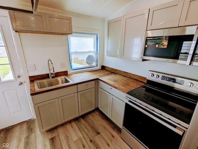 kitchen with wooden counters, stainless steel appliances, vaulted ceiling, sink, and light hardwood / wood-style floors