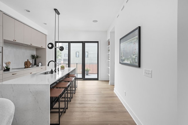 kitchen featuring a breakfast bar, sink, light hardwood / wood-style floors, pendant lighting, and light stone countertops