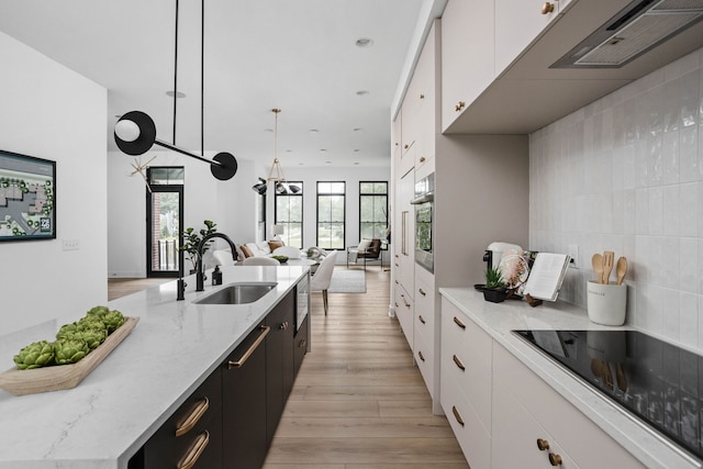 kitchen with sink, light wood-type flooring, black electric cooktop, hanging light fixtures, and stainless steel oven