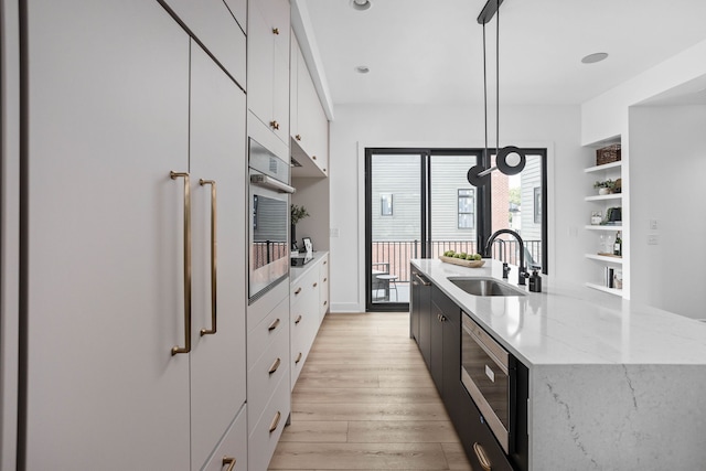 kitchen featuring pendant lighting, stainless steel appliances, sink, light stone counters, and light hardwood / wood-style floors