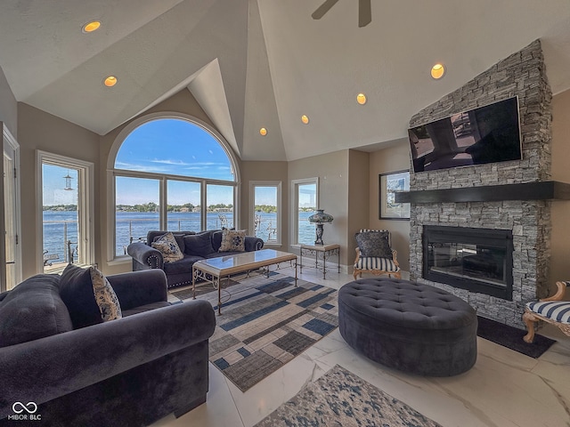 living room featuring a stone fireplace, tile flooring, ceiling fan, a water view, and high vaulted ceiling