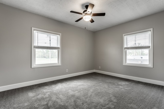 spare room featuring plenty of natural light, dark colored carpet, ceiling fan, and a textured ceiling