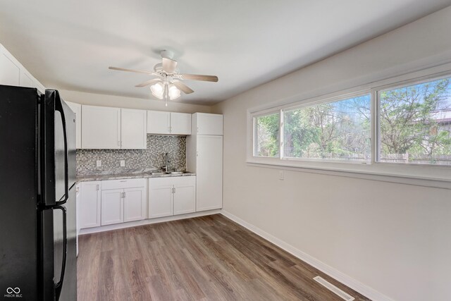 kitchen with decorative backsplash, hardwood / wood-style flooring, black fridge, and white cabinets