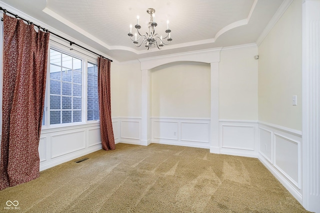 spare room with a raised ceiling, carpet floors, ornamental molding, and an inviting chandelier