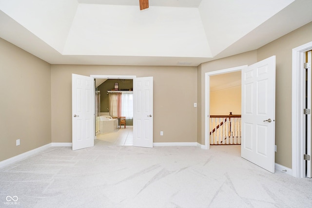 unfurnished bedroom featuring a raised ceiling, ensuite bathroom, and light colored carpet