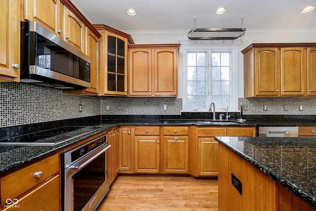 kitchen with sink, stainless steel appliances, light hardwood / wood-style flooring, dark stone counters, and ornamental molding