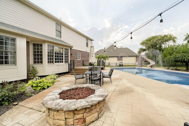 view of swimming pool with a water slide, a patio, a fire pit, and a deck