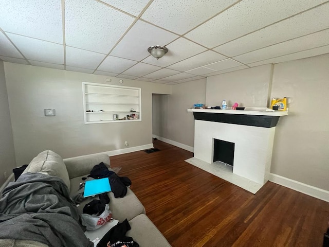 unfurnished living room with wood-type flooring, a paneled ceiling, and built in shelves