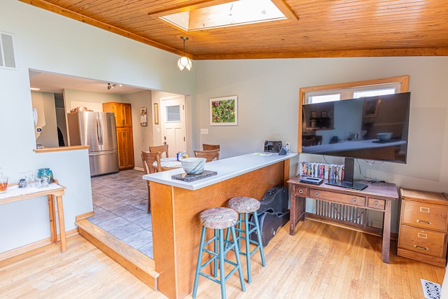 kitchen with kitchen peninsula, light wood-type flooring, a breakfast bar area, stainless steel fridge, and wooden ceiling