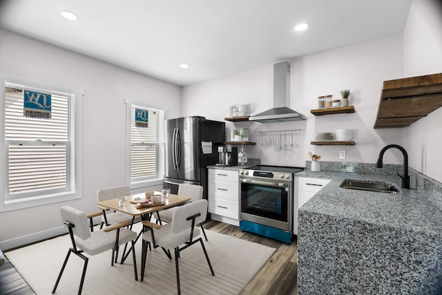 kitchen with plenty of natural light, appliances with stainless steel finishes, wall chimney range hood, and white cabinets