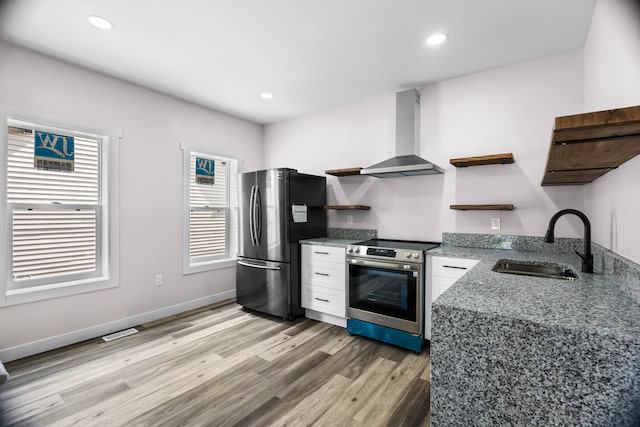 kitchen with white cabinetry, appliances with stainless steel finishes, wall chimney range hood, sink, and light hardwood / wood-style floors