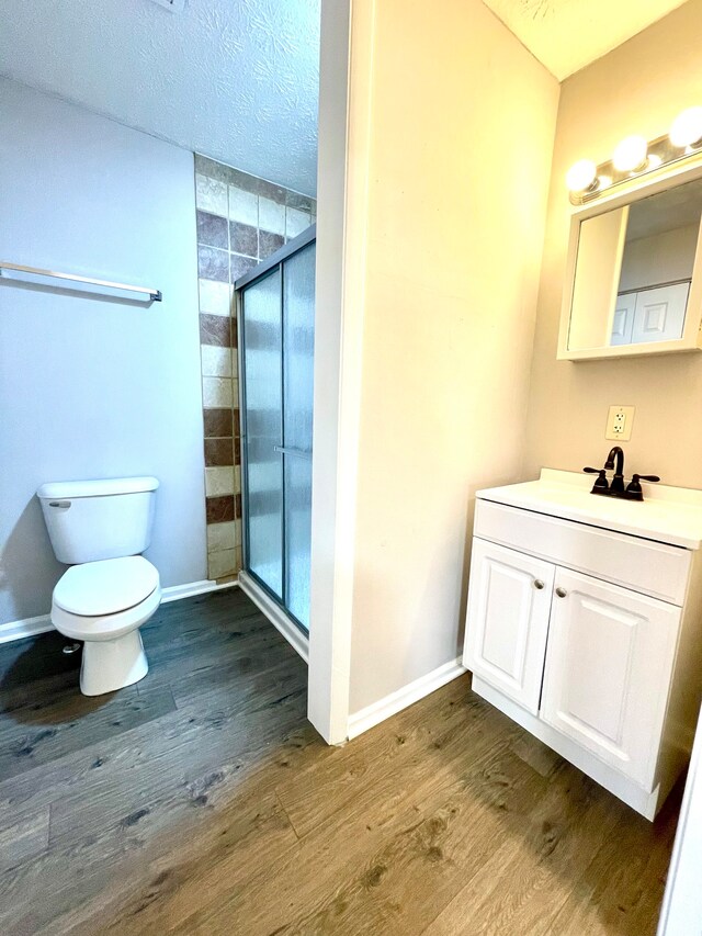 bathroom with hardwood / wood-style flooring, vanity, toilet, and a shower with door