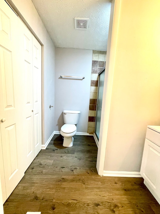 bathroom with a shower with shower door, wood-type flooring, vanity, toilet, and a textured ceiling