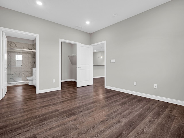 unfurnished bedroom with a closet, a spacious closet, dark hardwood / wood-style flooring, and ensuite bathroom