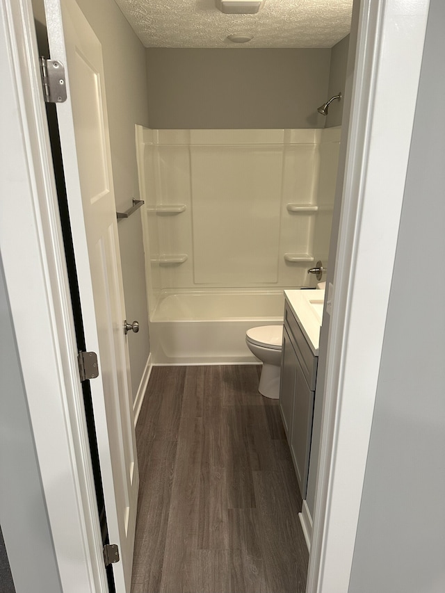 full bathroom featuring a textured ceiling, hardwood / wood-style flooring, toilet, vanity, and tub / shower combination