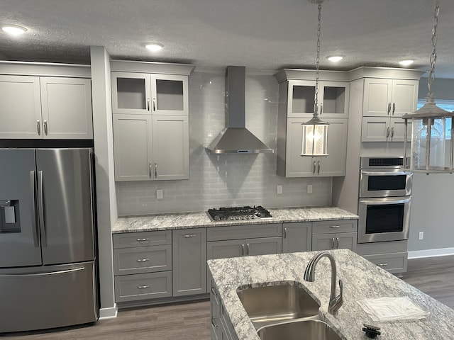 kitchen with sink, dark hardwood / wood-style flooring, hanging light fixtures, stainless steel appliances, and wall chimney exhaust hood