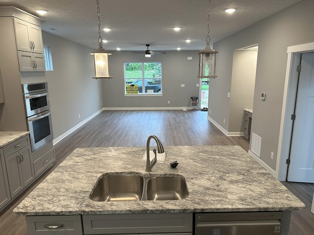 kitchen with appliances with stainless steel finishes, sink, gray cabinets, dark wood-type flooring, and a center island with sink