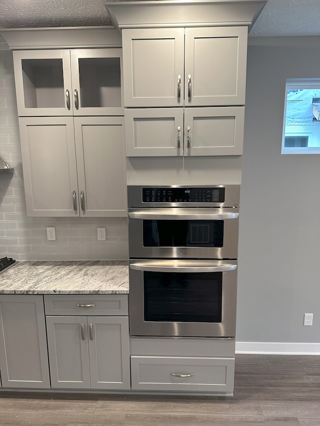 kitchen with light hardwood / wood-style floors, tasteful backsplash, light stone countertops, and double oven