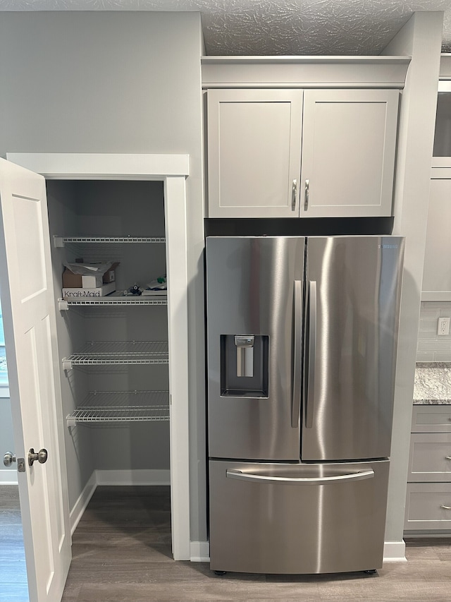 kitchen with light stone counters, hardwood / wood-style flooring, gray cabinets, and stainless steel fridge