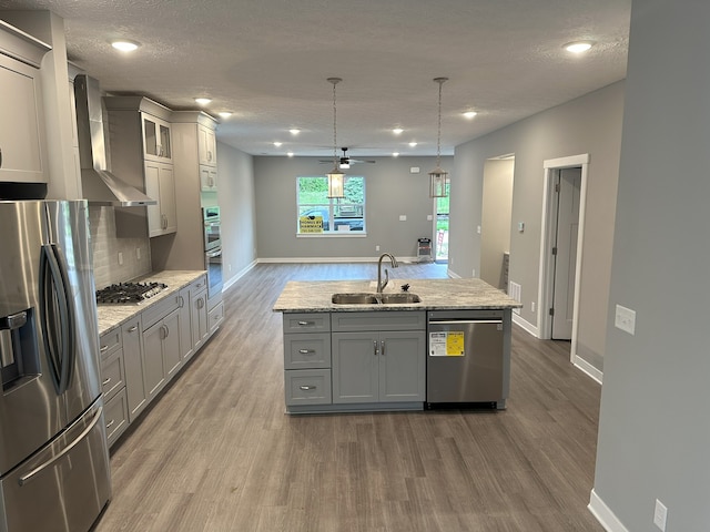 kitchen with sink, an island with sink, wall chimney range hood, and stainless steel appliances