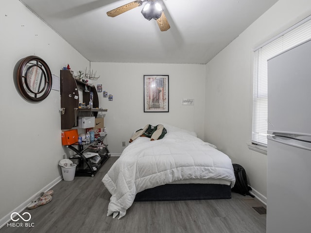 bedroom featuring white fridge, dark hardwood / wood-style flooring, and ceiling fan