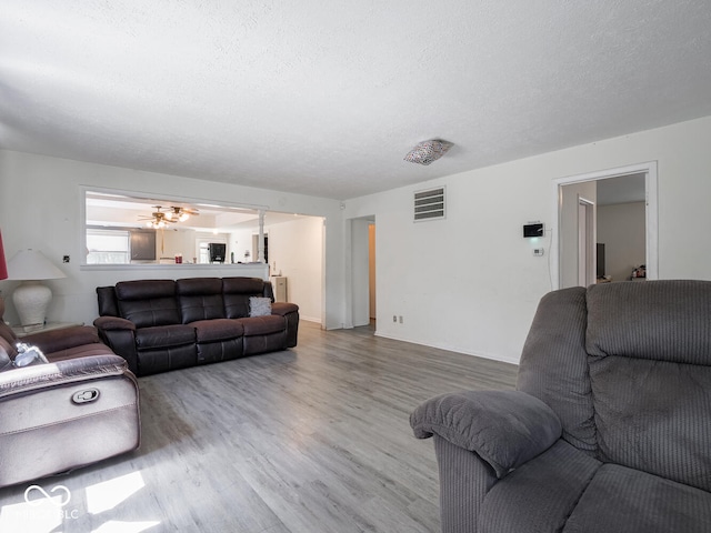 living room with a textured ceiling, ceiling fan, and hardwood / wood-style floors