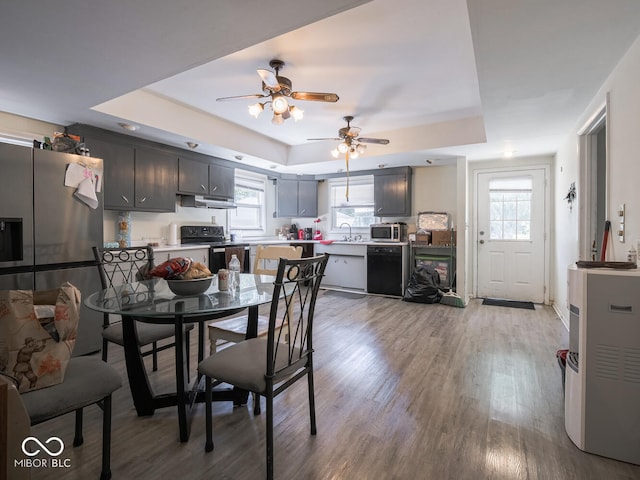 dining area featuring ceiling fan, hardwood / wood-style flooring, sink, and a tray ceiling