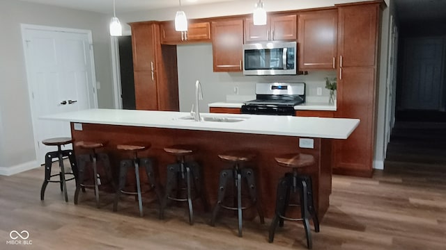 kitchen featuring dark hardwood / wood-style flooring, stainless steel appliances, sink, decorative light fixtures, and an island with sink